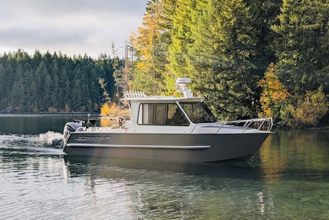 Kwigwis Adventures fishing charter boat anchored on calm water surrounded by dense evergreen forest under cloudy skies, showcasing the natural environment of Campbell River, BC.
